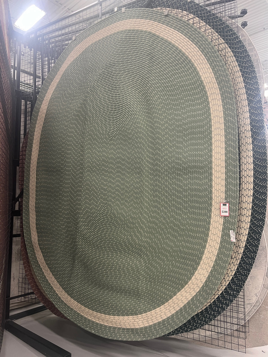Oval braided rug in sage green with cream border, made of polypropylene.