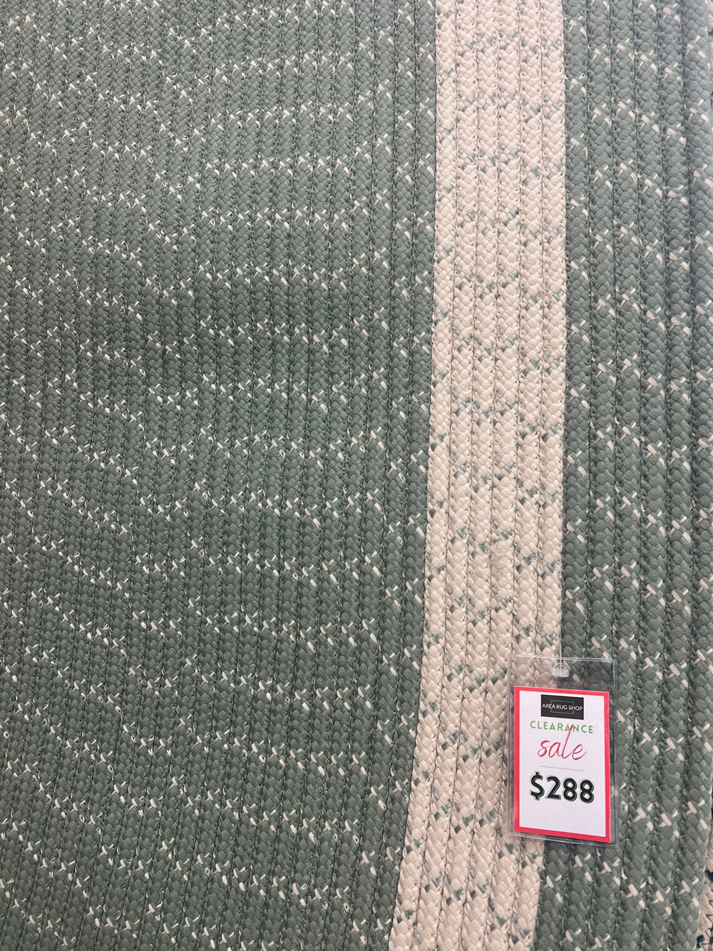 Close up Oval braided rug in sage green with cream border, made of polypropylene.