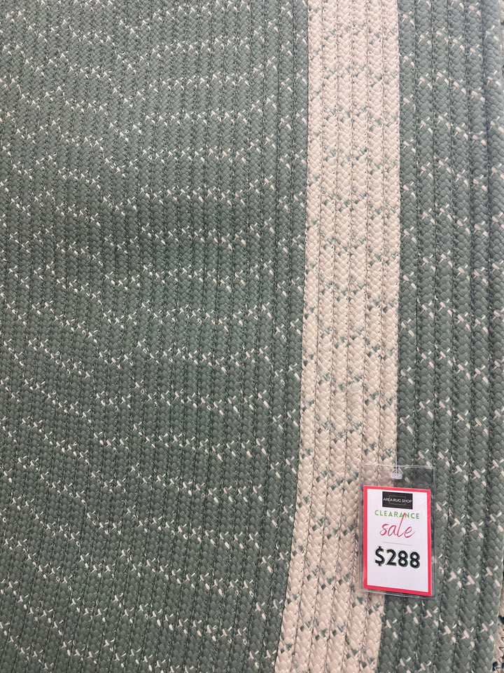 Close up Oval braided rug in sage green with cream border, made of polypropylene.