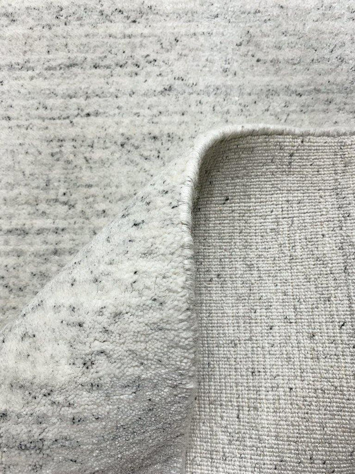 Akita Ivory Flek rug fold view white base dark grey flek horizontal texture